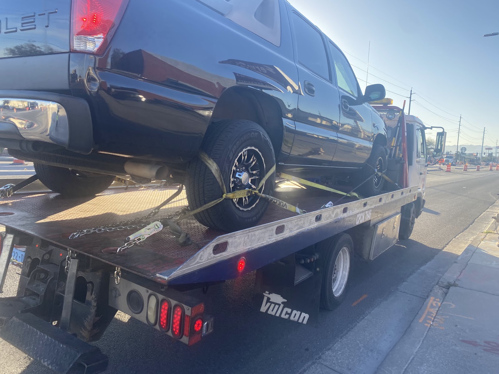 Black Chevrolet SUV strapped on a Vulcan flatbed tow truck in daylight