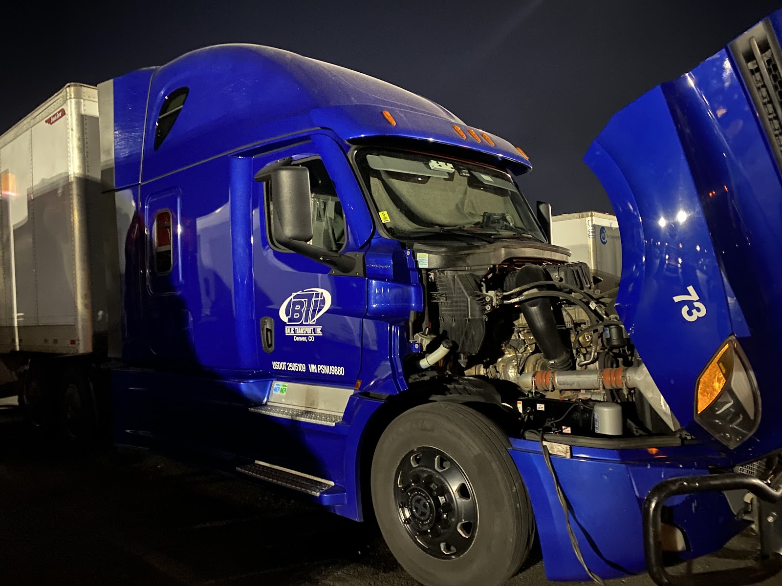 Blue BTI semi truck with hood open for engine repair at night